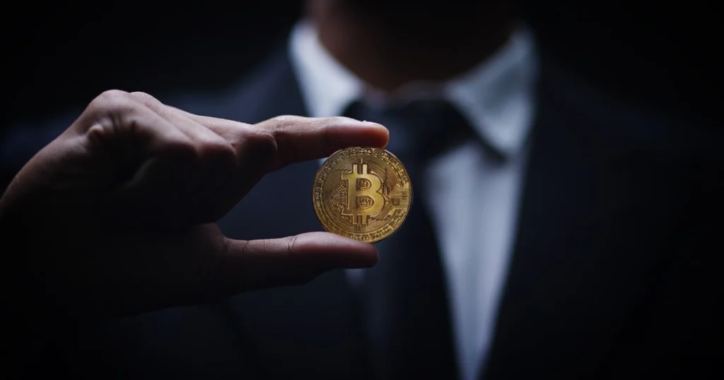 Man in a suit holding a Bitcoin coin in low light, underscoring that buying company stocks is not Bitcoin self-custody.